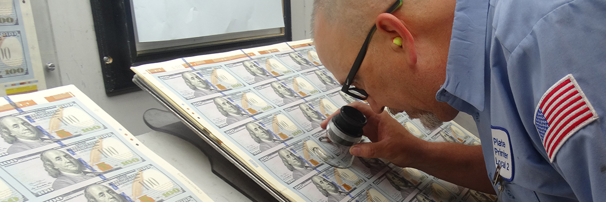 Man in uniform inspecting sheet of currency with magnifying glass