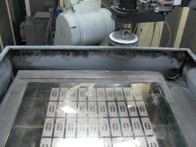 A $1 note 50-subject plate lies in the bed of a polishing device.