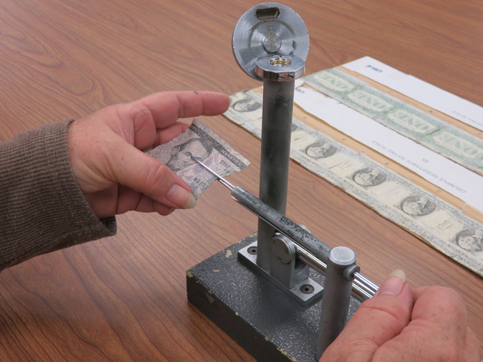 The Durability Laboratory performs a crumple test on a $5 note to assess ink flaking.