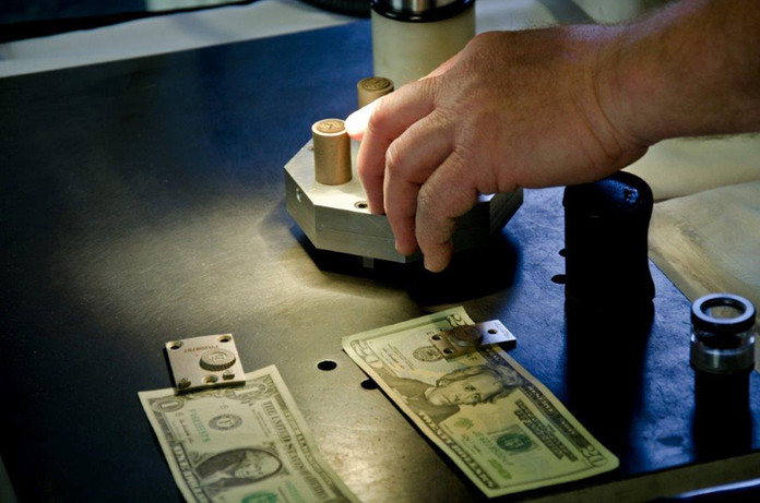 An intaglio plate maker inspects a graphite image of a Treasury Seal on the Electrical Discharge Machine.